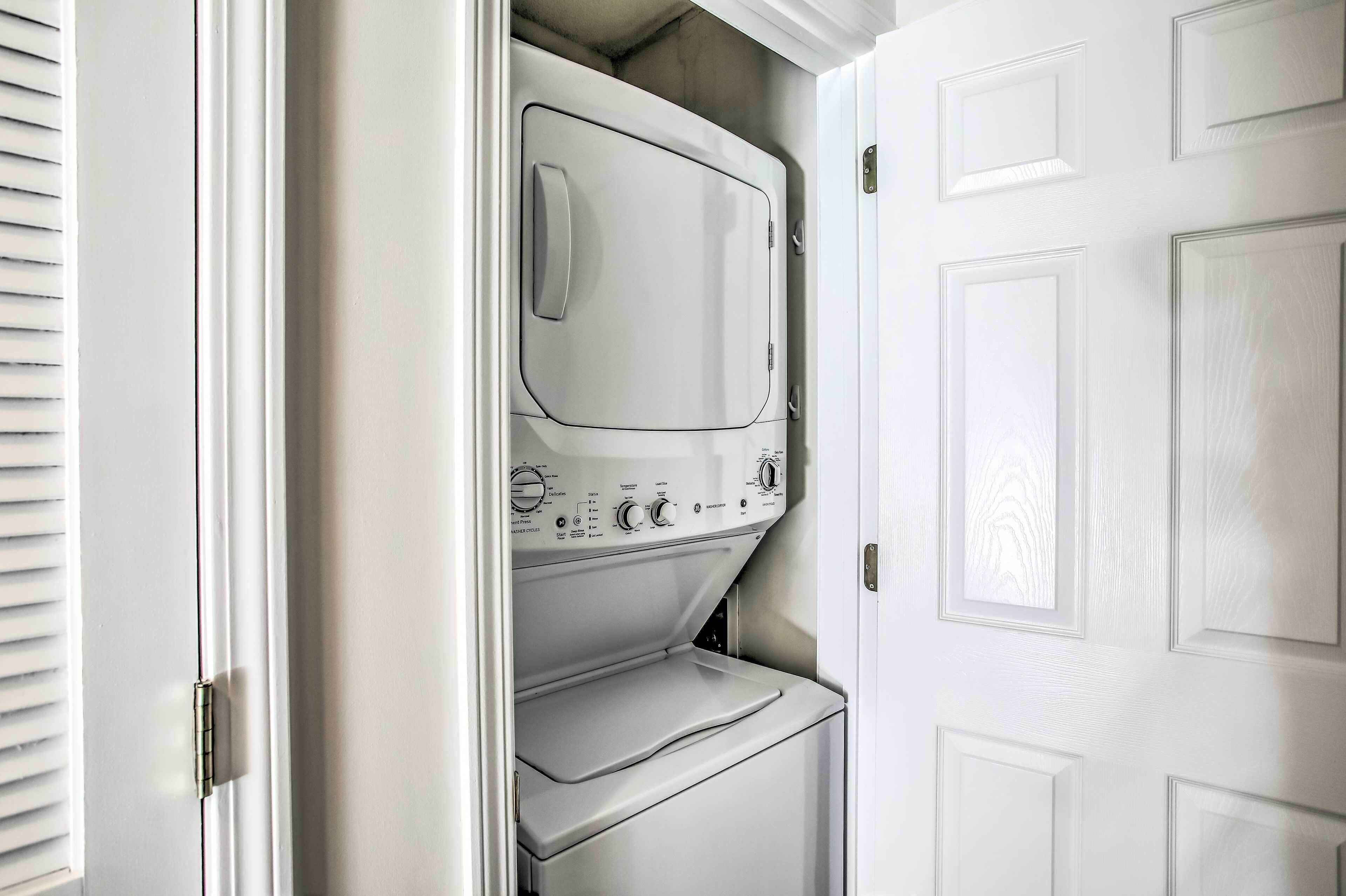 Un lavadero pequeño y blanco con lavadora y secadora integradas, una puerta con manija y una ventana con persianas.