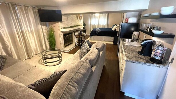 A compact living space with a sofa, a small dining area, a kitchen, and a fireplace. - Cozy Studio Guest Suite (Ames)