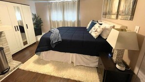 A bedroom with a bed, a nightstand, a lamp, a ceiling fan, a window with curtains, and a wardrobe. - Cozy Studio Guest Suite (Ames)