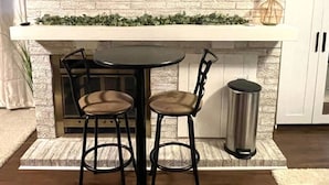 A kitchen with a brick wall, a white countertop, two bar stools, and a trash can. - Cozy Studio Guest Suite (Ames)