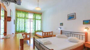 A bedroom with a wooden bed, a wooden desk, and a chair. There is a window with green curtains, a wall-mounted TV, and a painting on the wall.