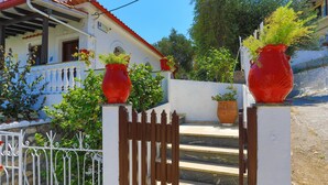 A white building with a red roof and a balcony. There are two large red vases with plants on the balcony.