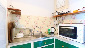 Una cocina con microondas, lavamanos y armarios verdes.