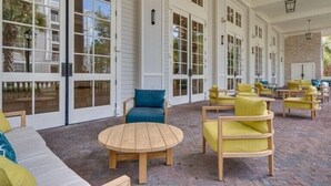 An outdoor patio area with wooden furniture, including a round table and chairs, and a sofa. - Enjoy This Elegant Coastal Condo:, King-Suite,Full kitchen,Pool, Hot Tub,Balcony (Miramar Beach)