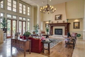 A spacious living room with a fireplace, large windows, and a chandelier.