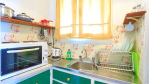 Una cocina con microondas, lavamanos y escurreplatos. Hay ollas en la encimera y una ventana con cortinas.