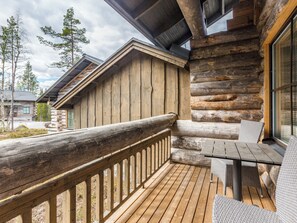 Een houten terras met een glazen balustrade, een tafel met stoelen en uitzicht op de omliggende bomen.