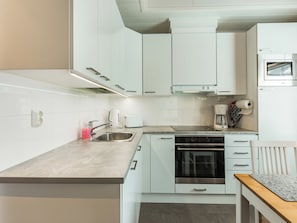 Een moderne keuken met witte kastjes, een roestvrijstalen spoelbak, een ingebouwde oven en een magnetron.