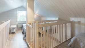 Ein Schlafzimmer im Dachgeschoss mit hohen Decken, Holzboden, weißen Wänden und einem weißen Geländer.