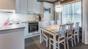 Eine moderne Küche mit weißen Schränken, einem Holztisch und einem großen Fenster mit Jalousien.