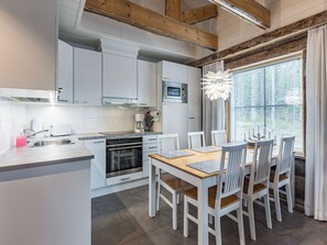 Une cuisine moderne avec des meubles blancs, un four encastré et un coin repas comprenant une table en bois et des chaises blanches.