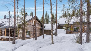 Eine Blockhütte mit schneebedecktem Dach, umgeben von hohen Kiefern.