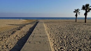 A beach with a paved walkway leading to the sea, palm trees, and clear skies. - Nice apartment for 4 people with WIFI, TV and terrace (Torredembarra)