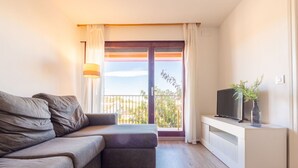 A modern living room with a grey sofa, a small TV on a white cabinet, and a balcony with a view of greenery. - Nice apartment for 4 people with WIFI, TV and terrace (Torredembarra)