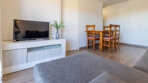 A modern living room with a flat-screen TV on a white console, a dining table with four wooden chairs, and a grey sofa. - Nice apartment for 4 people with WIFI, TV and terrace (Torredembarra)