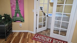 Una sala de bugaderia amb una porta que condueix a una zona de servei, un quadre amb la Torre Eiffel i un felpú amb la inscripció "Laundry Room".