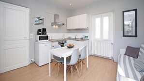 A compact kitchen with white cabinetry, a dining table with chairs, a stove, and a microwave.