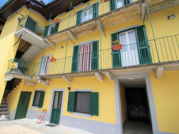 Un edificio amarillo con persianas verdes, balcones con barandillas y una puerta.