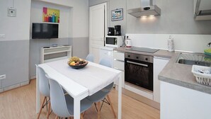 A modern kitchen with a built-in oven, microwave, and coffee maker. A dining table with chairs and a bowl of fruit is in the center.