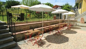 An outdoor patio with stone flooring, wooden tables, red metal chairs, and white umbrellas. - Lovely apartment for 3 people with WIFI, TV and patio (Germignaga)
