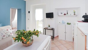 A modern kitchen with white cabinets, a tiled floor, a flat-screen TV, and a small table with a basket of oranges. - Lovely apartment for 3 people with WIFI, TV and patio (Germignaga)
