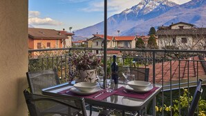Un balcone con un tavolo apparecchiato per mangiare, con vista su un paesaggio montuoso e case sullo sfondo.