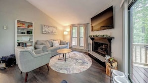 A modern living room with a fireplace, a sofa, a coffee table, and a bookshelf. - Cozy Pet-Friendly w Fire Pit, Wifi & Pool Access (Hedgesville)