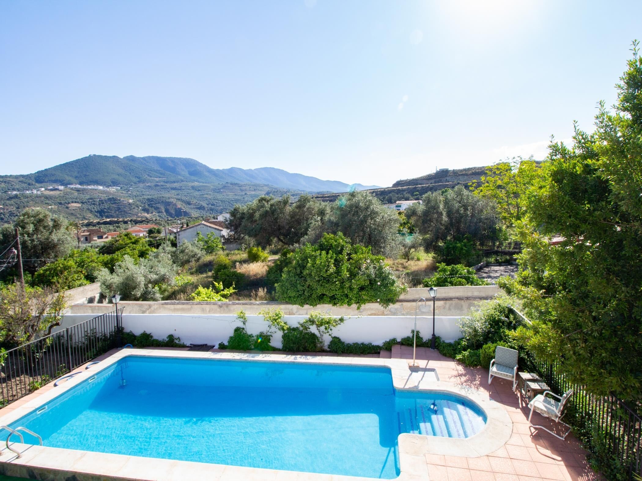 Une piscine rectangulaire à l’eau d’un bleu limpide, entourée d’une terrasse carrelée et d’une clôture en métal.