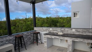A modern outdoor kitchen with a stone backsplash, two stools, and a bench. - This brand new Villa, modern amenities,  Pool deck and ocean views (Ceder Village)