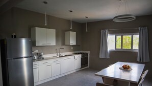 A modern kitchen with white cabinets, a stainless steel refrigerator, a gas stove, and a dining table with chairs. - This brand new Villa, modern amenities,  Pool deck and ocean views (Ceder Village)