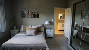 A bedroom with a large bed, bedside tables, a nightstand, a lamp, a mirror, and a painting on the wall. - This brand new Villa, modern amenities,  Pool deck and ocean views (Ceder Village)