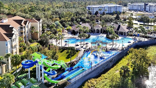 Een resort met een groot zwembad, glijbanen en meerdere gebouwen.