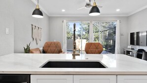 Een moderne keuken met een wit aanrecht, twee bruine fauteuils, een zwarte hanglamp en een plafondventilator.