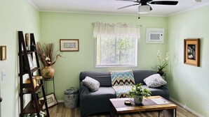 A living room with a dark green sofa, a wooden coffee table, a ceiling fan, and a window with blinds. - Puakenikeni Hilo Hale (Hilo)
