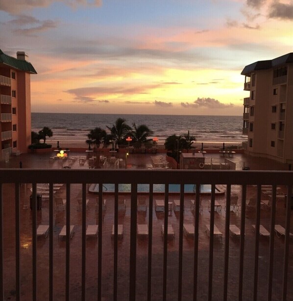 A beachfront view from a balcony with lounge chairs and a pool area.