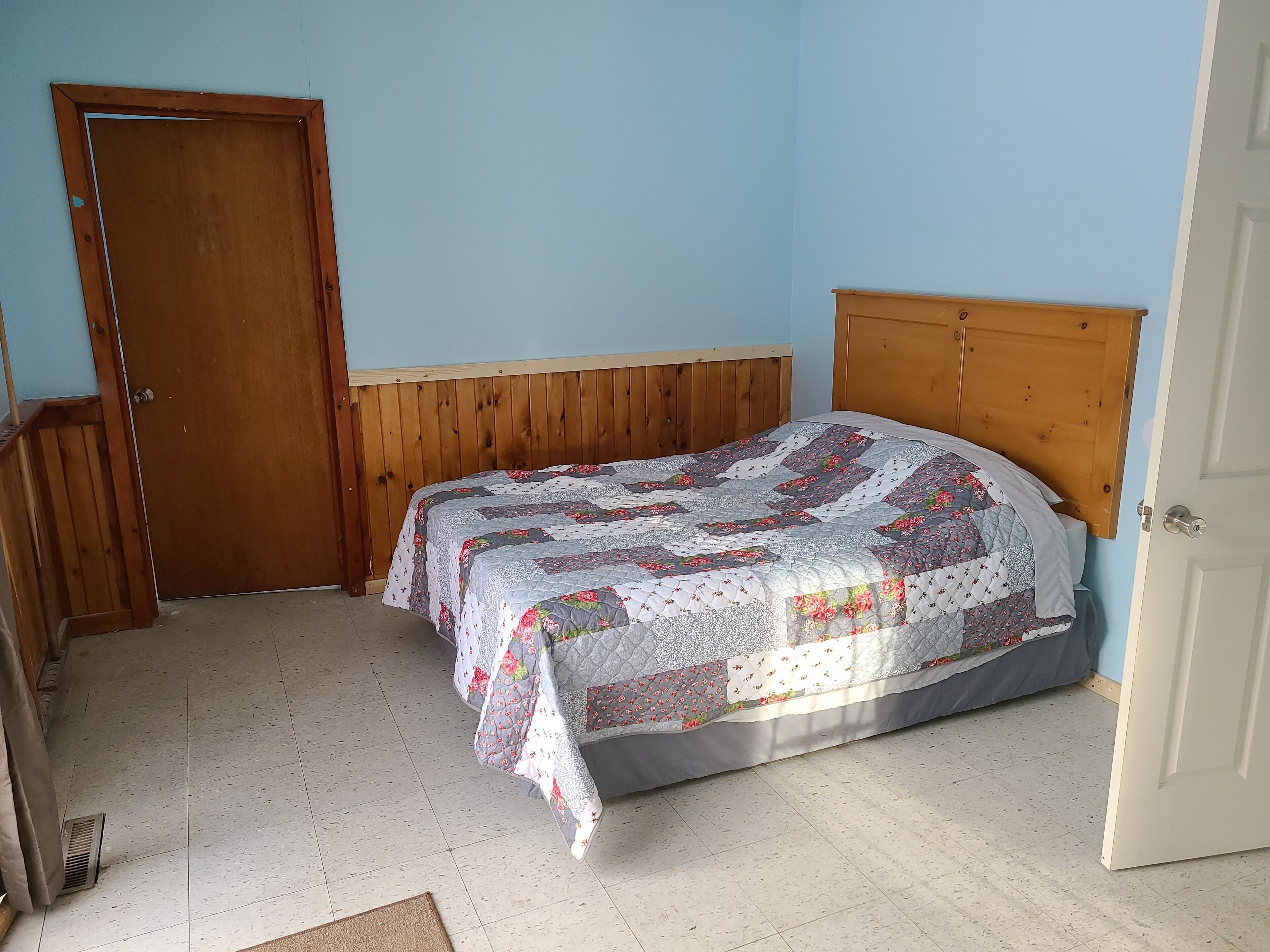 Een slaapkamer met een houten hoofdbord, een gewatteerde spreideken en een deur.