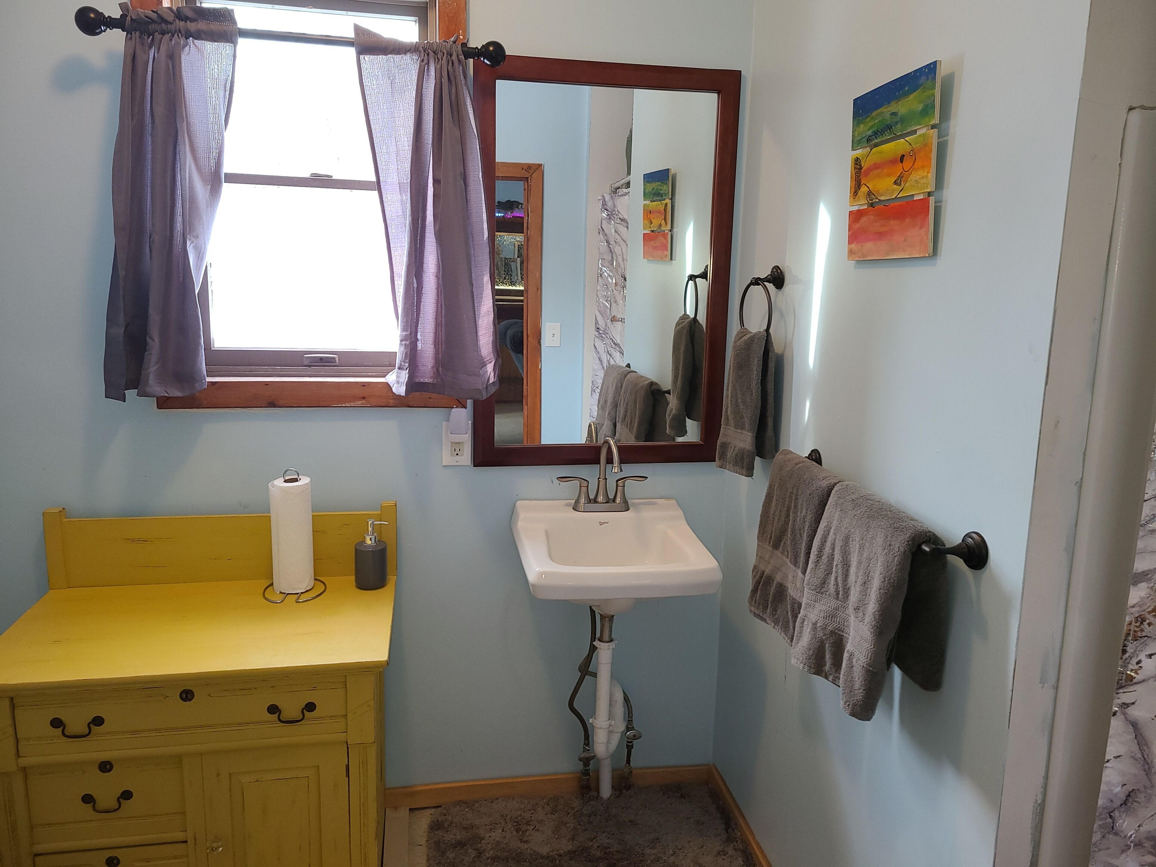 Un baño con un tocador amarillo, un lavabo blanco, un espejo y toallas colgadas en un perchero.