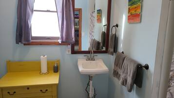 Un baño con un tocador amarillo, un lavabo blanco, un espejo y toallas colgadas en un perchero.