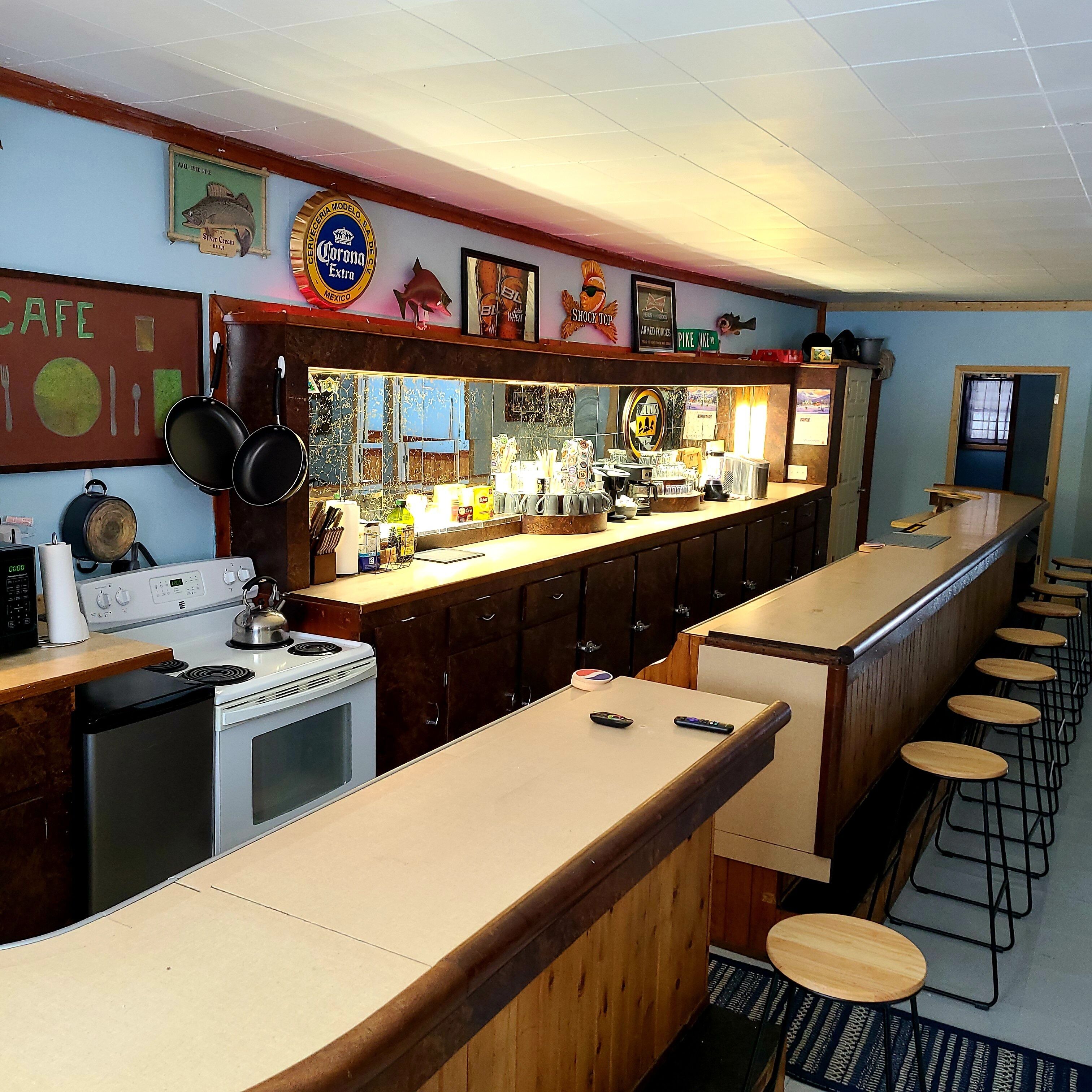 A bar area with a long counter, stools, a stove, and various kitchen items.