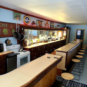 A bar area with a long counter, stools, a stove, and various kitchen items. - Jake's Bed & Bar 3BR, 7 beds, SXS Snowmobile Trail Access, Fire Pit, Grill, Wifi (Toivola)