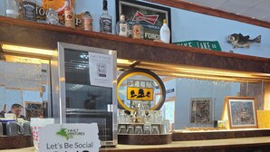 Een bar met een QR-code voor sociale media, verschillende drankflessen en een ingelijste foto van een vis aan de muur.
