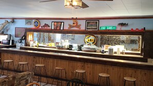 Een restaurantinterieur met een bar, houten barstoelen en een plafondventilator.
