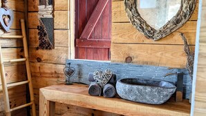 Une salle de bain rustique en bois, avec un banc en bois, un lavabo en pierre et un miroir en forme de cœur.
