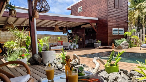 Une terrasse extérieure avec une table en verre, deux boissons et une chaise en bois.