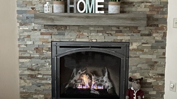 A fireplace with a stone wall backdrop, a shelf with plants and the word "HOME", and a teddy bear on the mantel.