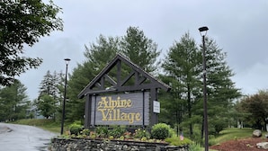 A wooden sign for Alpine Village with a stone border and a flag.
