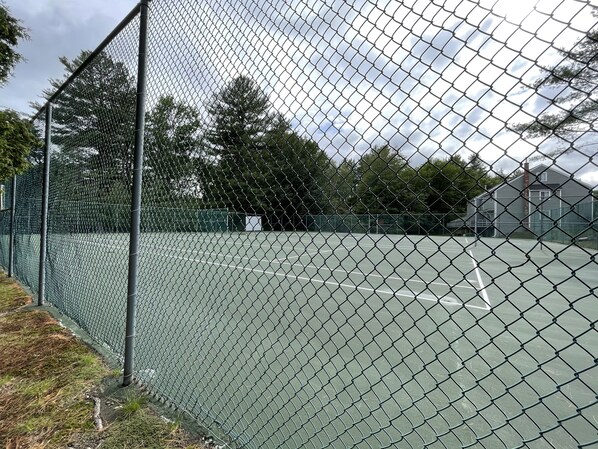A chain-link tennis court surrounded by a metal fence.