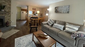 A living room with a sofa, coffee table, and a fireplace. There is a dining area with a table and chairs in the background.
