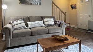 A living room with a grey sofa, a wooden coffee table, and a painting of a tree on the wall.