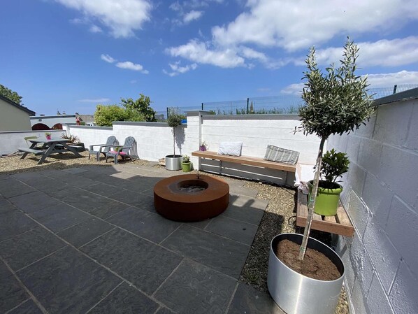A rooftop patio with a fire pit, seating area, and potted plants.